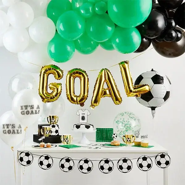 Football themed party setup with green, black, and white decorations, GOAL balloon banner, football print tableware, and balloons arranged around a party table